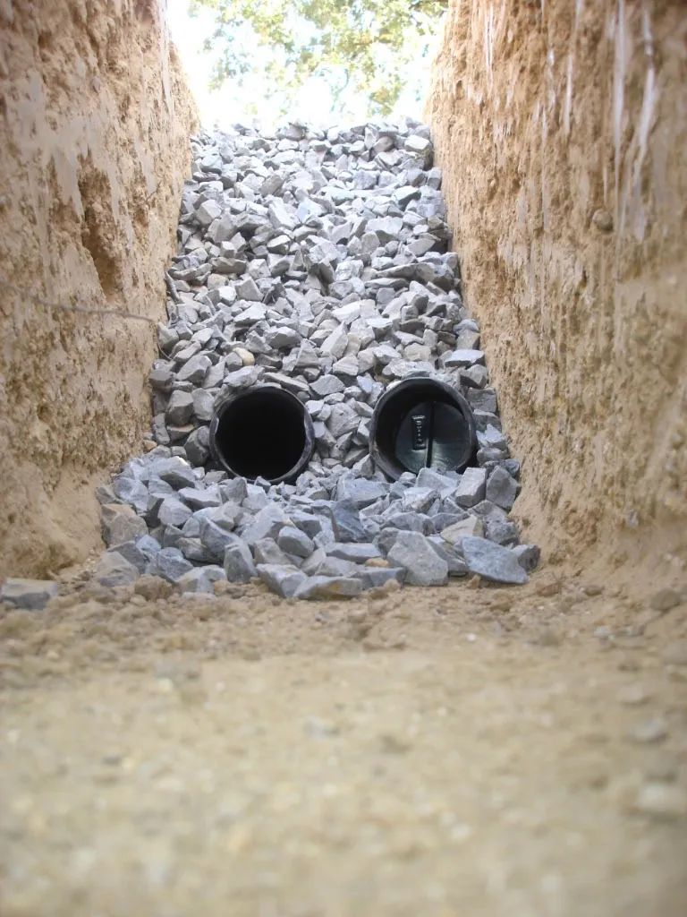 Two perforated drain pipes in gravel-filled trench during french drain installation